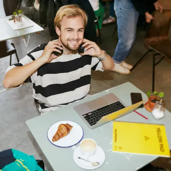 Student zit aan tafel met zijn laptop en bord met een croissant